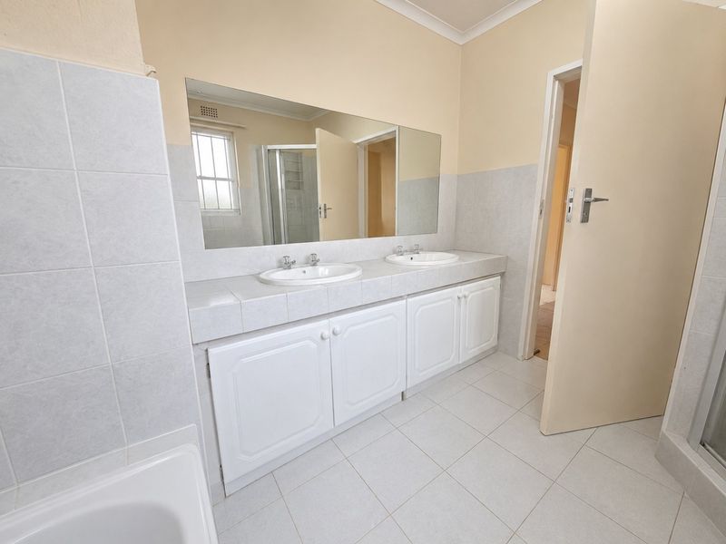 A clean and functional bathroom featuring a double vanity with white cabinetry, large wall mirror, and neutral floor tiling.