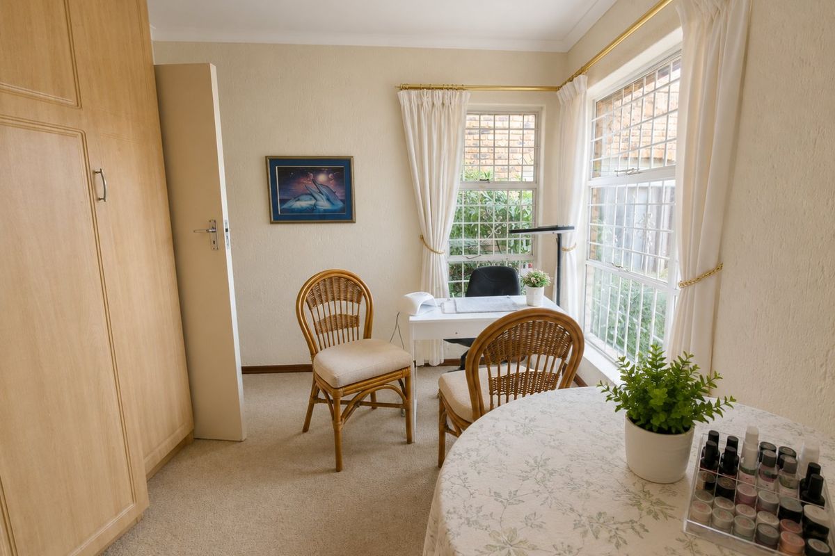 A bedroom featuring built-in wardrobes, carpeted flooring, and large windows with security bars, currently utilized as a home office or salon space.