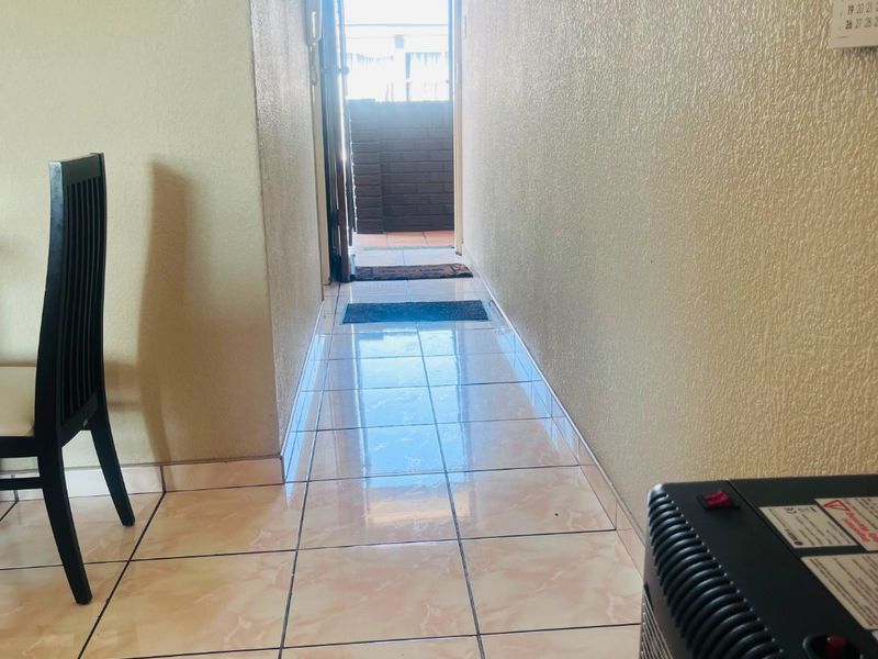 A narrow hallway with light-colored tiled flooring leading towards an exterior doorway, providing access to the outdoor area.