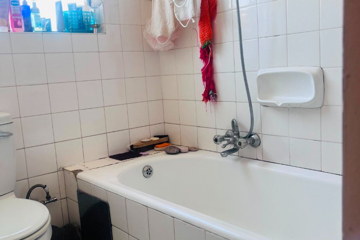 A dated bathroom featuring a standard bathtub, shower mixer, and toilet, requiring significant cosmetic updates and repairs to the wall finishes and tiling.