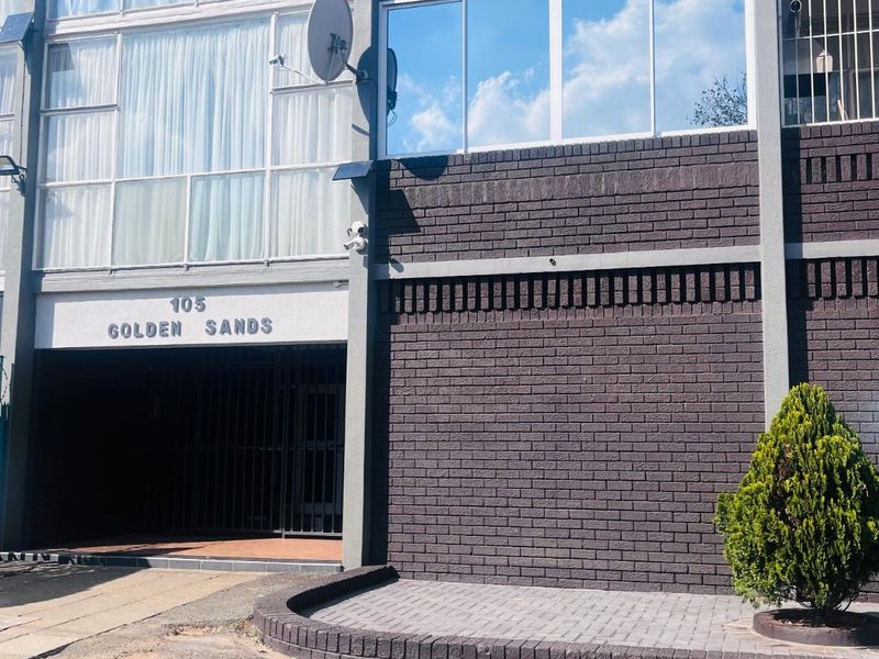 Front facade of the Golden Sands townhouse complex featuring dark brickwork, large sliding windows, and a secure gated entrance.