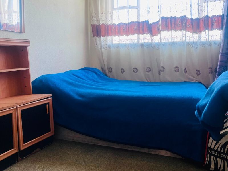 A bedroom featuring carpeted flooring and a window with curtains, showing signs of wear and requiring cosmetic updates to the walls and ceiling.