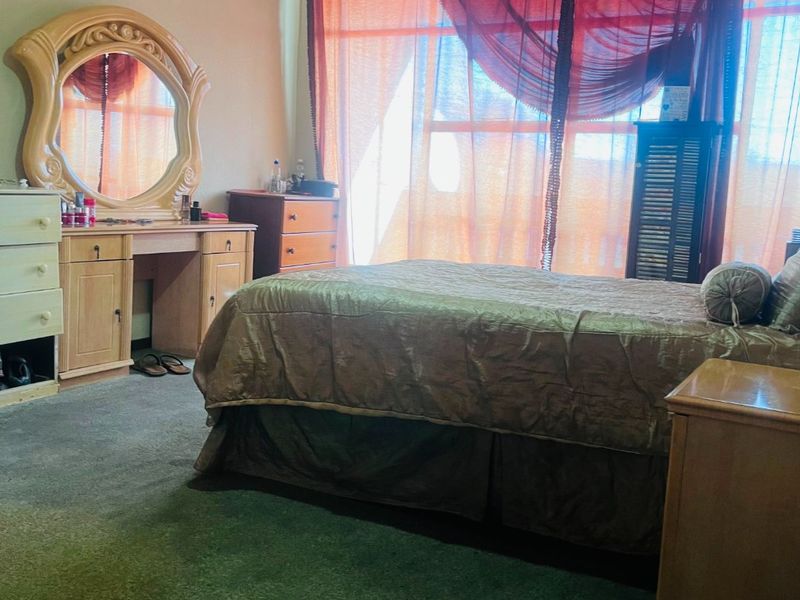A bedroom featuring carpet flooring and a large window, providing natural light. The space would benefit from cosmetic updates to modernize the finishes.