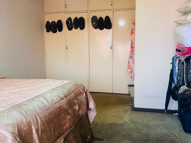 A bedroom featuring built-in cupboards with overhead storage and carpeted flooring, requiring cosmetic updates to modernize the space.