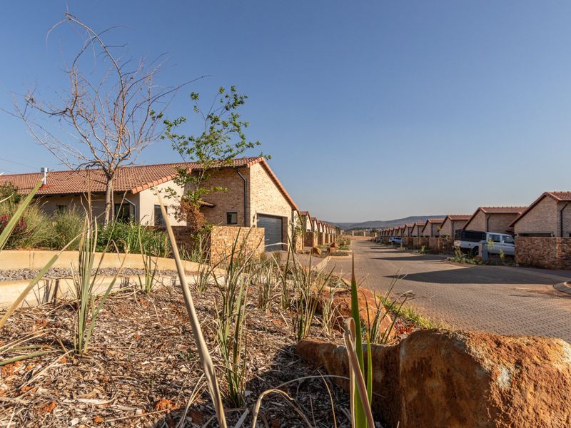 A street-level view of a residential townhouse complex featuring uniform facebrick facades, tiled roofs, and paved driveways within a well-maintained estate setting.