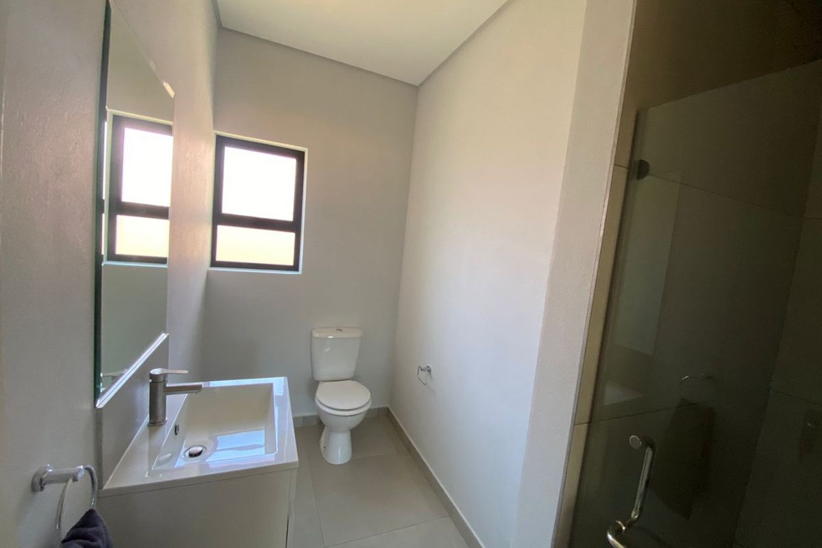 A clean, modern bathroom featuring a vanity with basin, a toilet, and a glass-enclosed shower with neutral floor tiling.