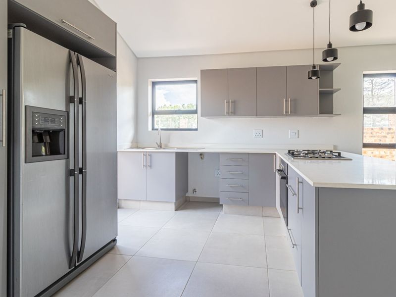 Modern kitchen featuring sleek grey cabinetry, stone countertops, a gas hob, built-in oven, and contemporary pendant lighting in a bright, open-plan layout.