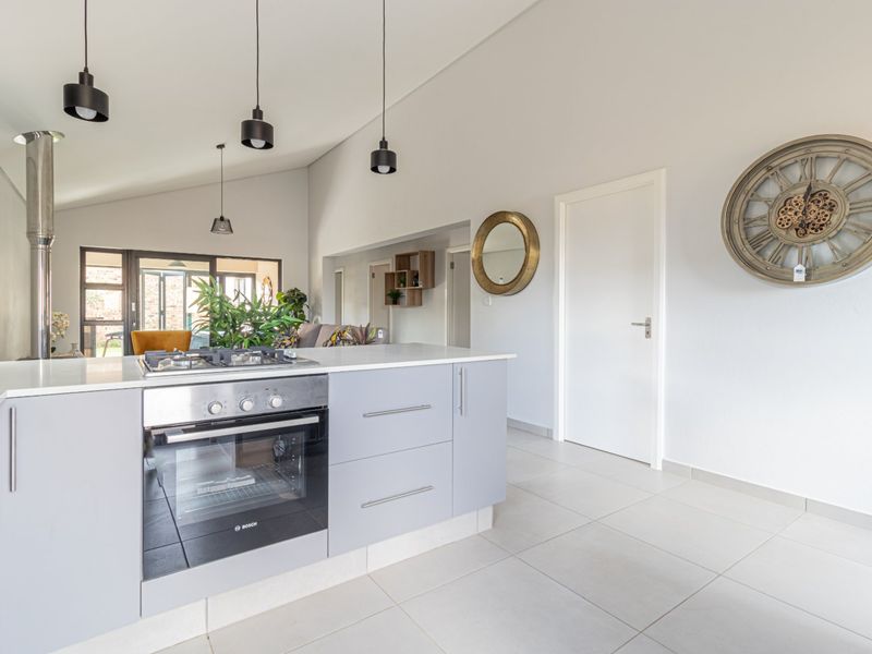 Modern open-plan living area featuring a sleek kitchen island with built-in oven and gas hob, vaulted ceilings, and neutral tiled flooring throughout.