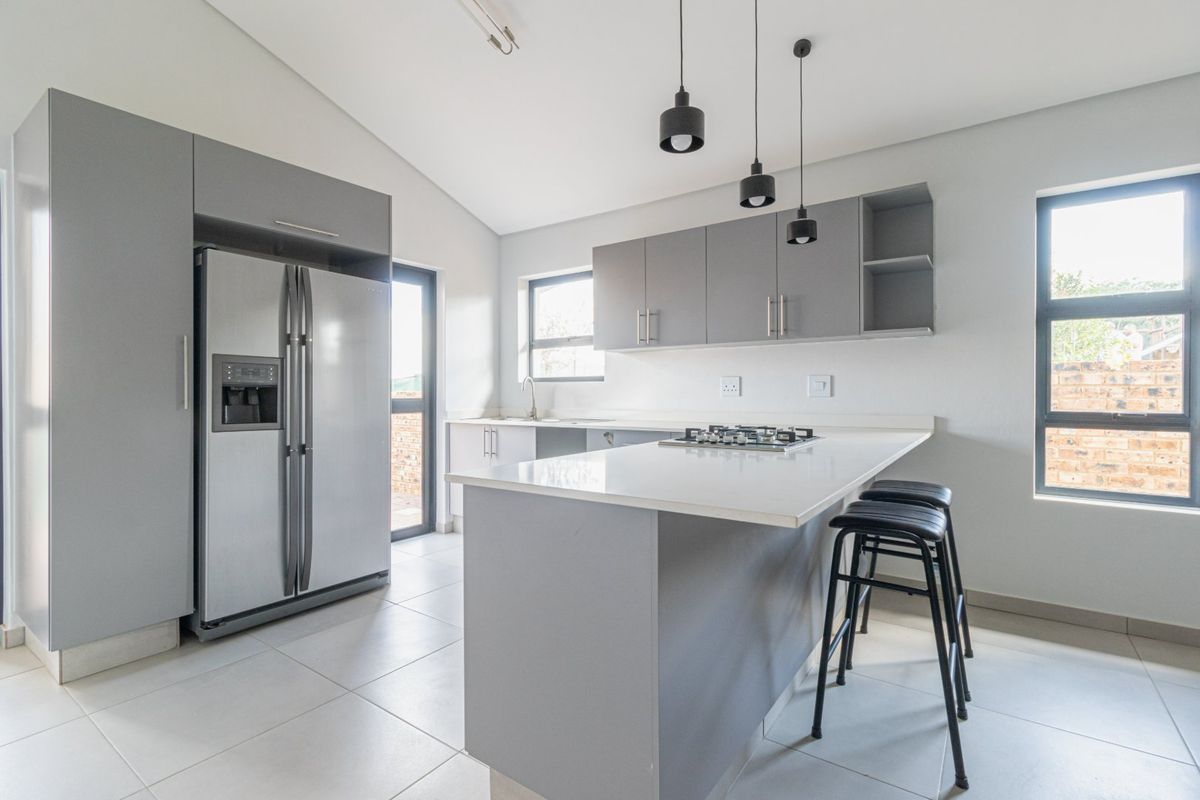 Modern kitchen featuring sleek grey cabinetry, stone countertops, a gas hob, and contemporary pendant lighting, offering a clean and functional culinary space.