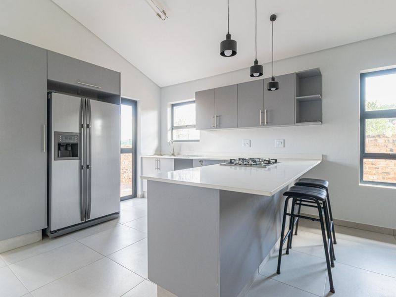 Modern kitchen featuring sleek grey cabinetry, stone countertops, a gas hob, and contemporary pendant lighting, offering a clean and functional culinary space.
