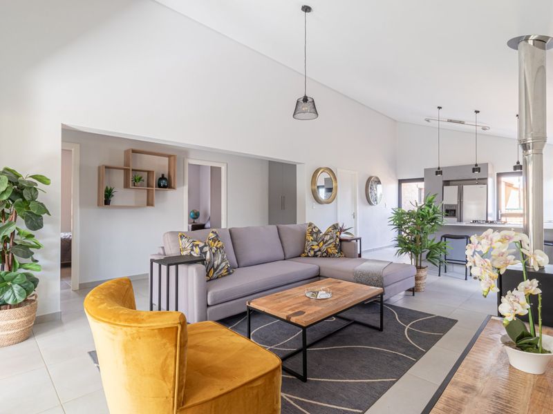 Spacious open-plan living area featuring a vaulted ceiling, tiled floors, a modern kitchen with an island, and a central freestanding fireplace.