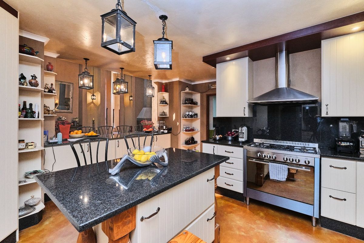 A well-appointed kitchen featuring a central island with granite countertops, stainless steel gas stove, extractor fan, and ample built-in cabinetry with open shelving.