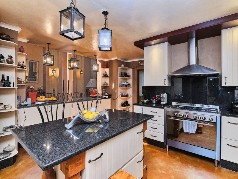 A well-appointed kitchen featuring a central island with granite countertops, stainless steel gas stove, extractor fan, and ample built-in cabinetry with open shelving.