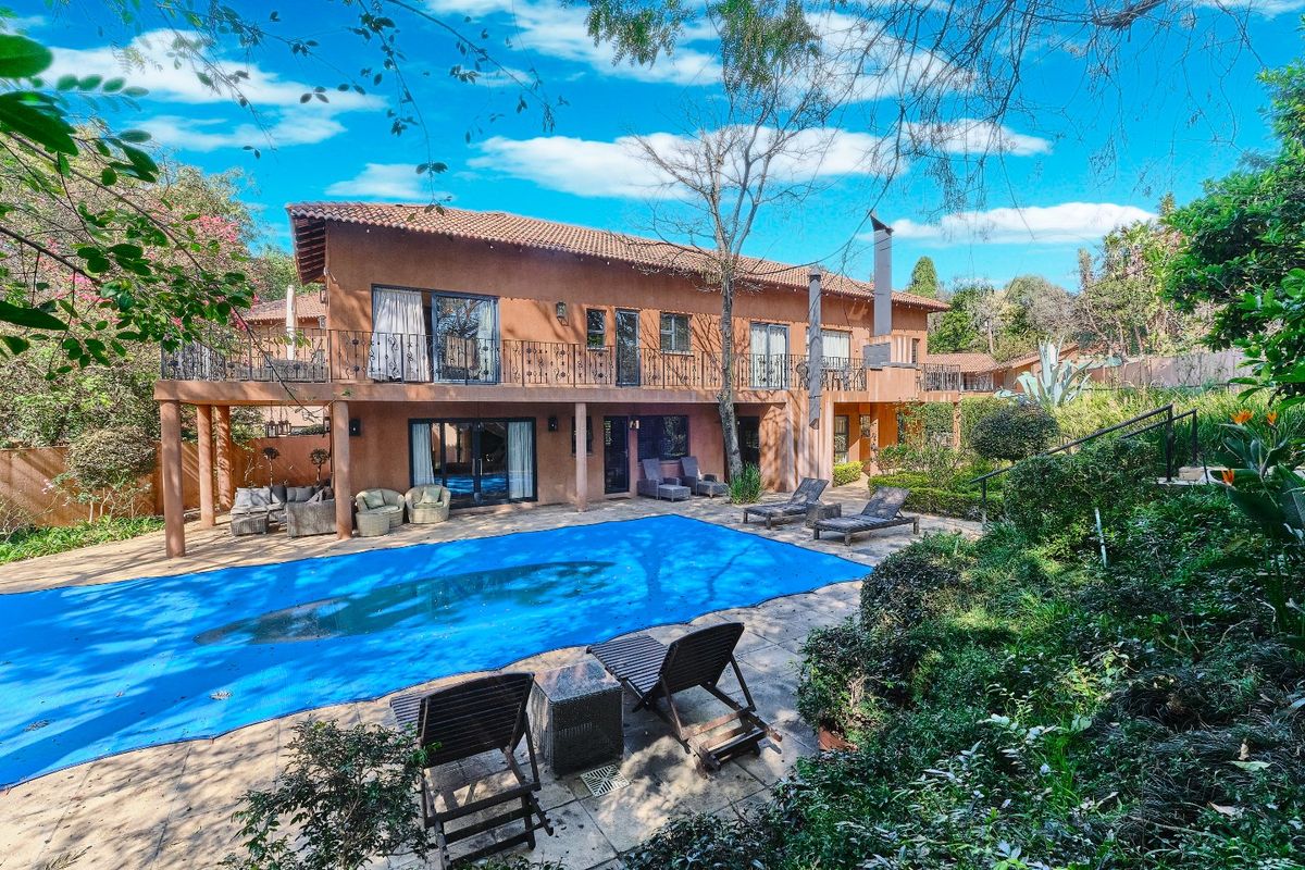 Rear view of a two-story house featuring a swimming pool, covered patio, and a spacious balcony with wrought iron railings overlooking the garden.