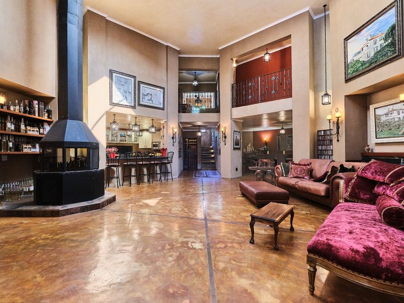 Spacious open-plan living area featuring a central freestanding fireplace, polished concrete floors, a built-in bar, and a mezzanine level with wrought iron railings.