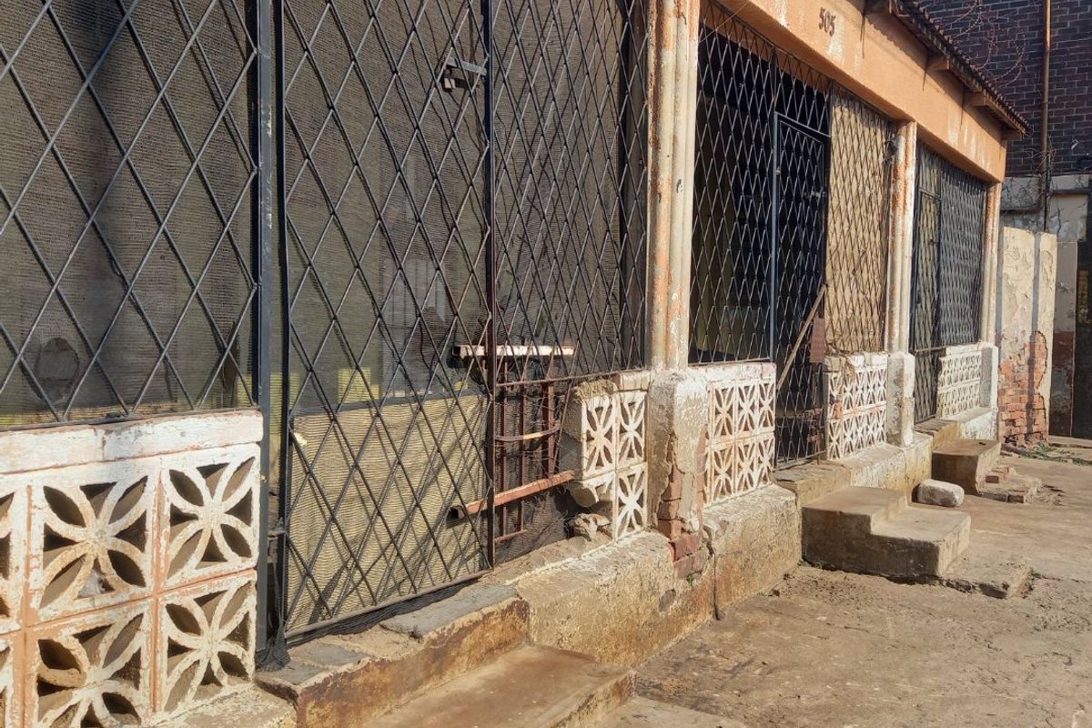 Rear exterior view of a property featuring security gates, breeze block detailing, and concrete steps, showing significant signs of wear and weathering.