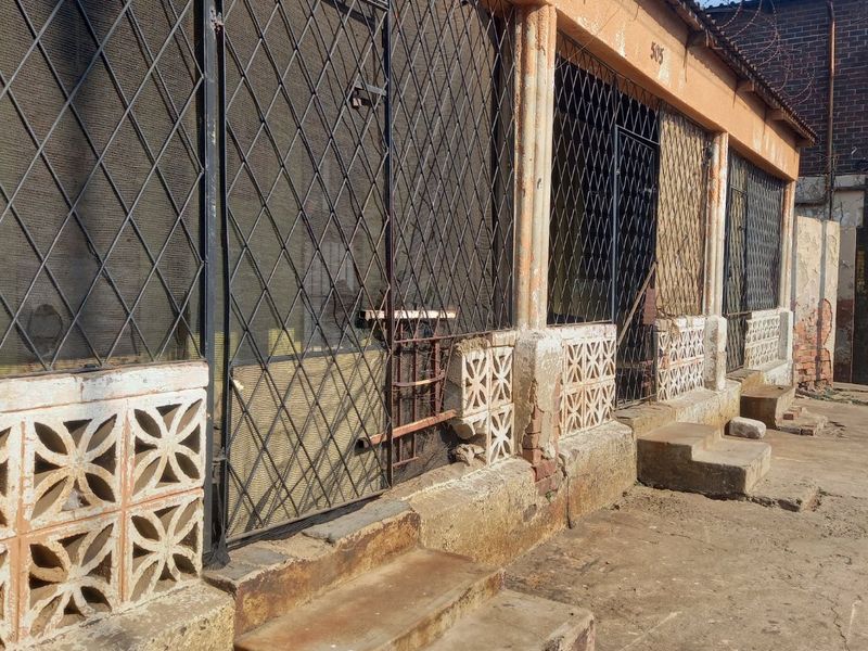 Rear exterior view of a property featuring security gates, breeze block detailing, and concrete steps, showing significant signs of wear and weathering.
