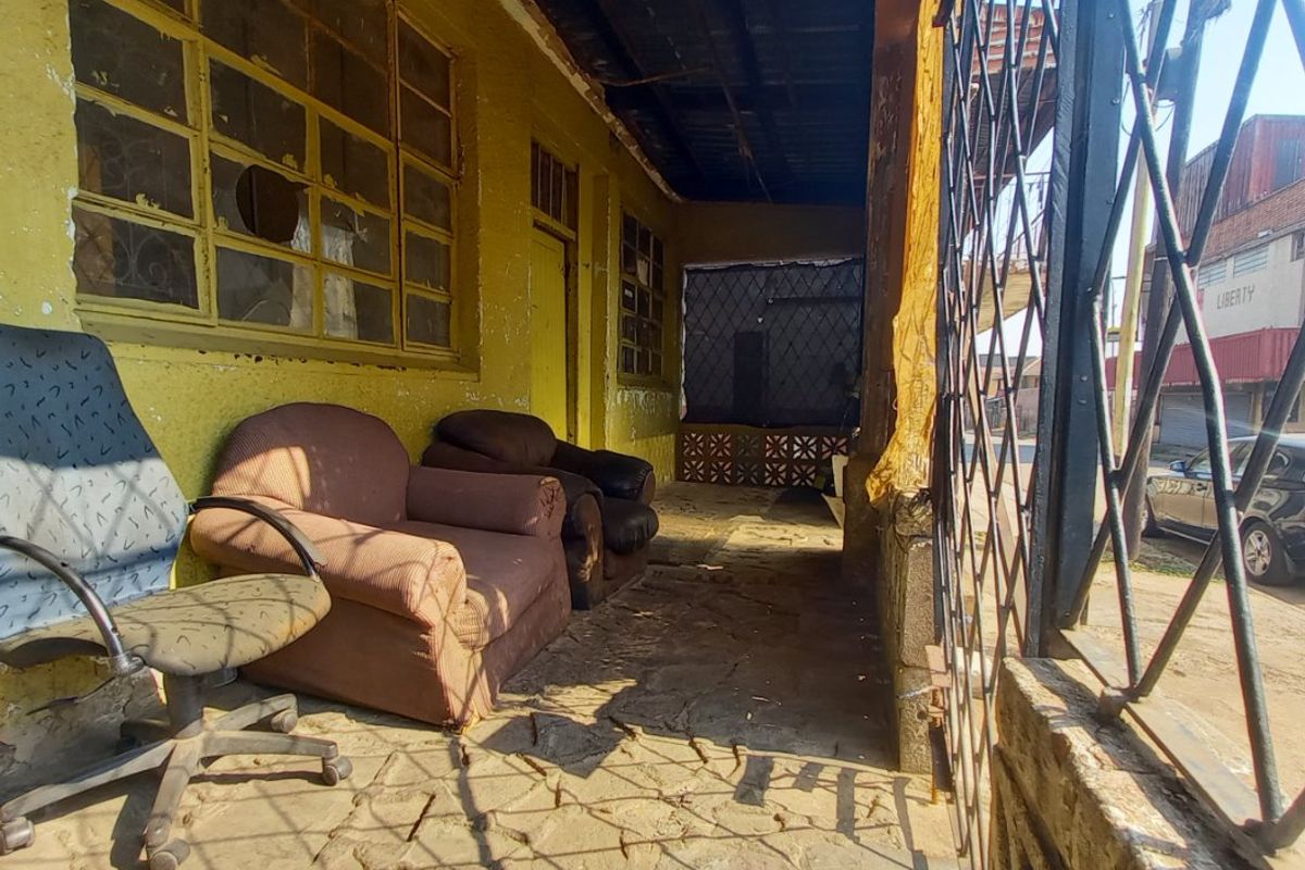 A covered outdoor patio area featuring stone flooring and metal security screening, showing significant signs of wear and requiring maintenance.