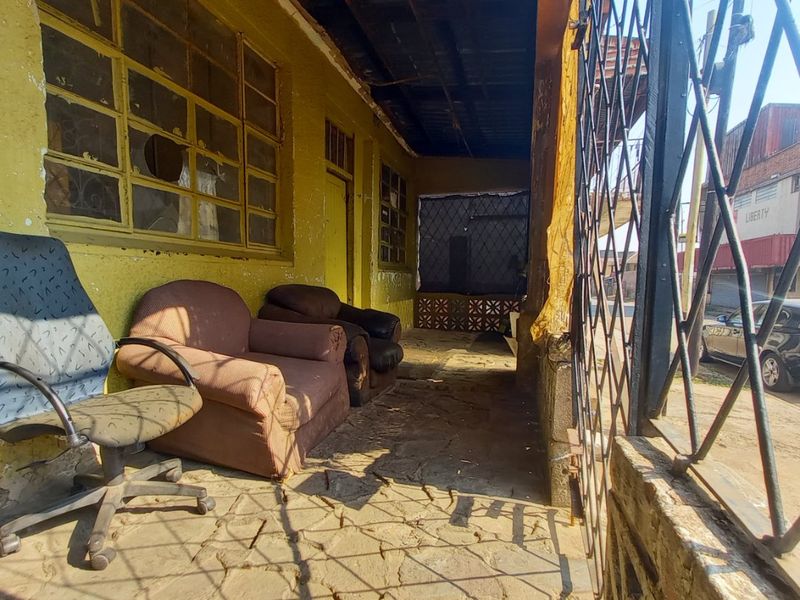 A covered outdoor patio area featuring stone flooring and metal security screening, showing significant signs of wear and requiring maintenance.