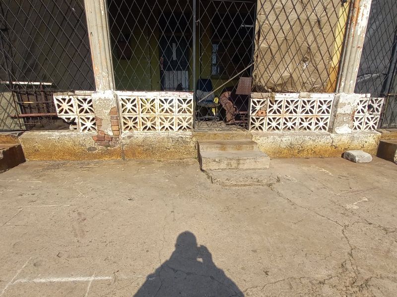 A weathered outdoor patio area featuring decorative breeze block walls, concrete flooring, and metal security screening in need of significant maintenance and restoration.