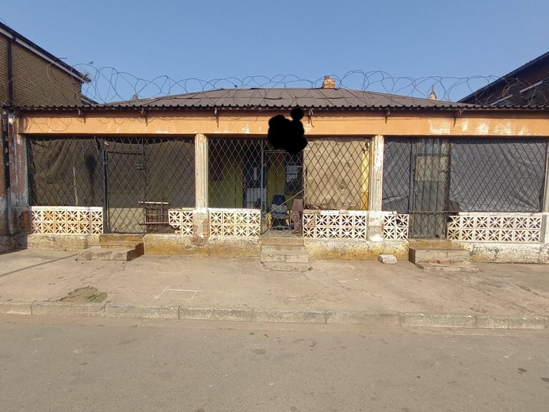 Front elevation of a residential property featuring security gates, breeze block detailing, and perimeter razor wire fencing.