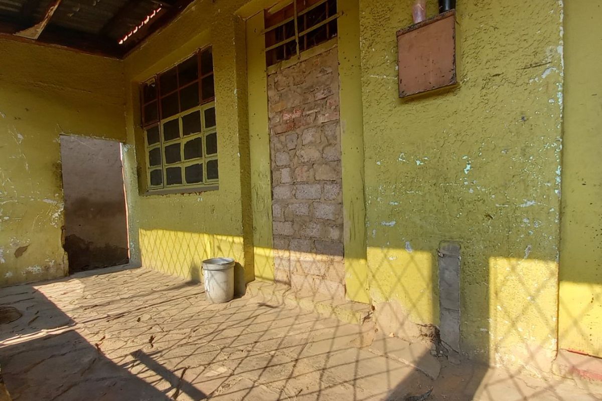 A covered outdoor patio area featuring stone flooring, a corrugated metal roof, and walls requiring maintenance and repainting.