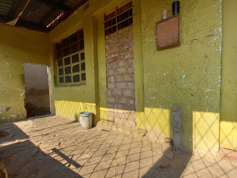 A covered outdoor patio area featuring stone flooring, a corrugated metal roof, and walls requiring maintenance and repainting.