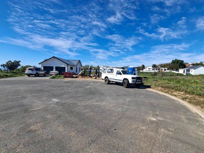 A street-level view of a vacant residential plot featuring paved road access and surrounding neighborhood infrastructure.