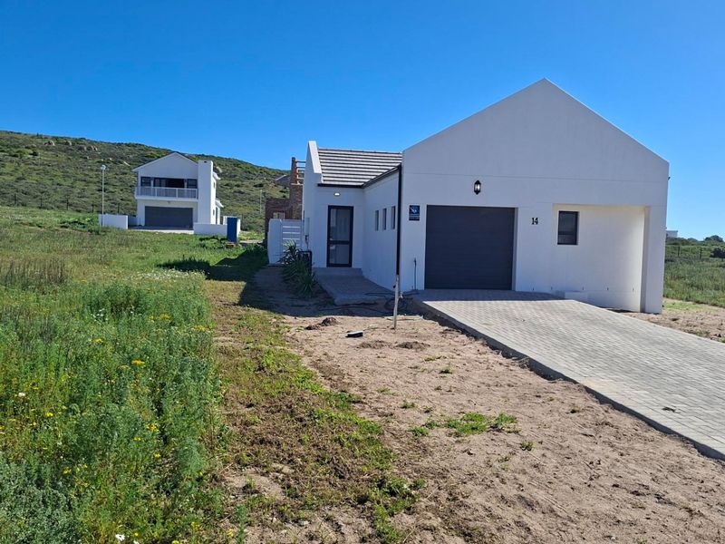 Front view of a modern residential property featuring a paved driveway, single garage, and white exterior finish in a coastal landscape setting.