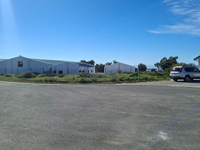 View of the property frontage featuring an asphalt driveway, paved verge, and surrounding industrial-style structures.