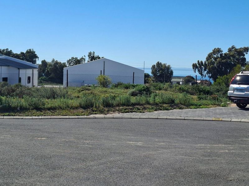 A view of a vacant residential plot featuring paved driveway access, kerbing, and surrounding fencing with distant coastal views.