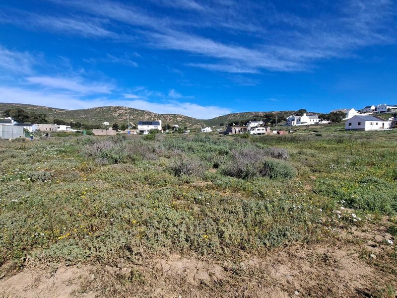 A wide-angle view of a vacant residential plot featuring natural coastal vegetation with surrounding neighborhood homes in the background.