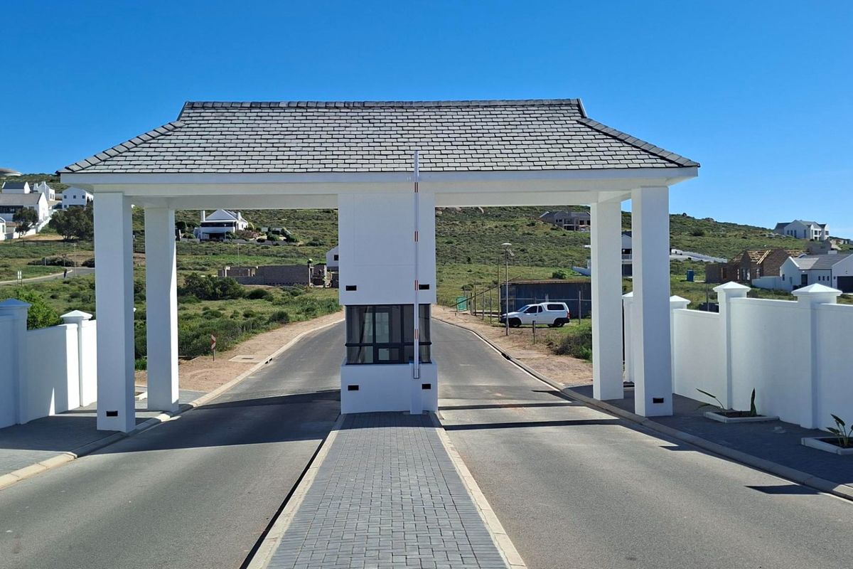 A well-maintained residential estate entrance featuring a modern security gatehouse, paved driveway, and perimeter boundary walls under a clear sky.