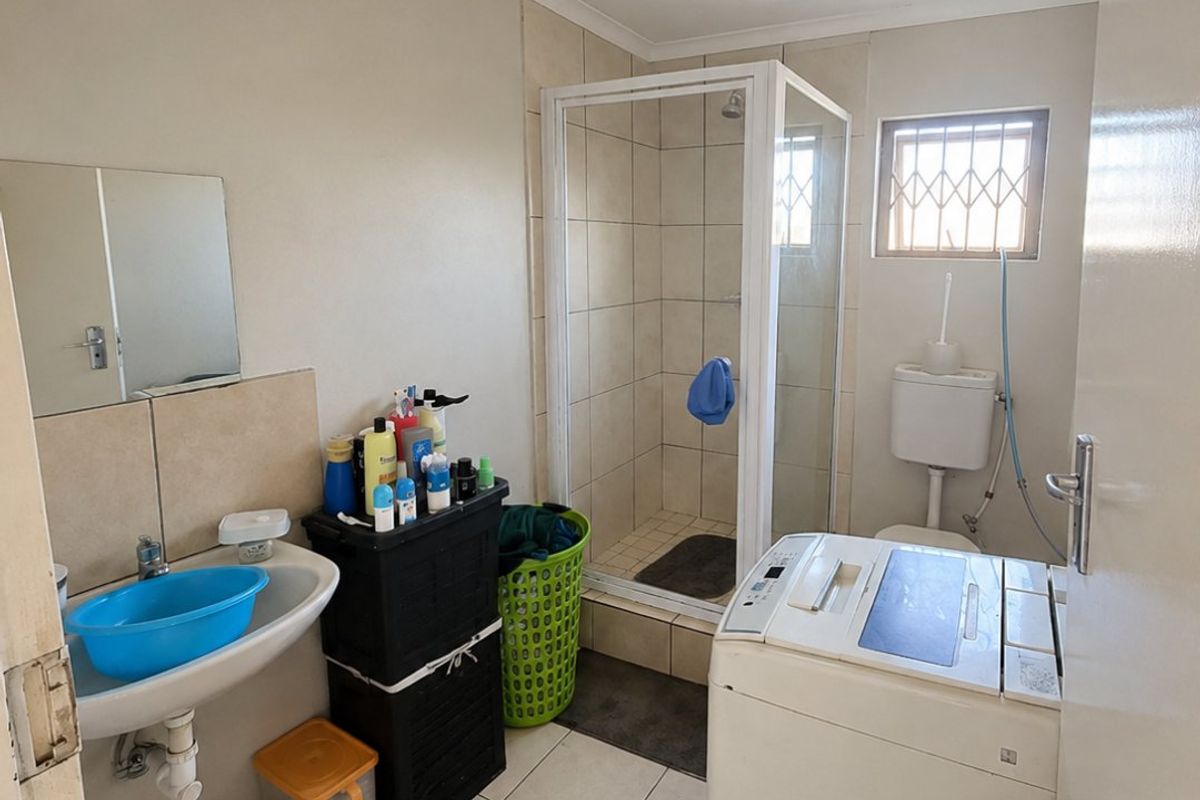 Functional bathroom featuring a shower enclosure, wall-mounted basin, and toilet, with tiled flooring and a security-fitted window.
