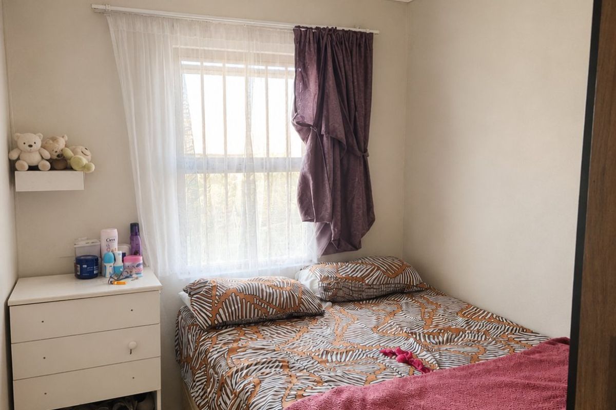 A compact bedroom featuring tiled flooring, a window with security bars, and a central ceiling light fixture.