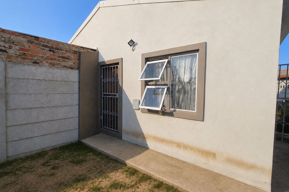 Rear exterior view of the property featuring a security gate, top-hung window, and concrete walkway along the base of the wall.