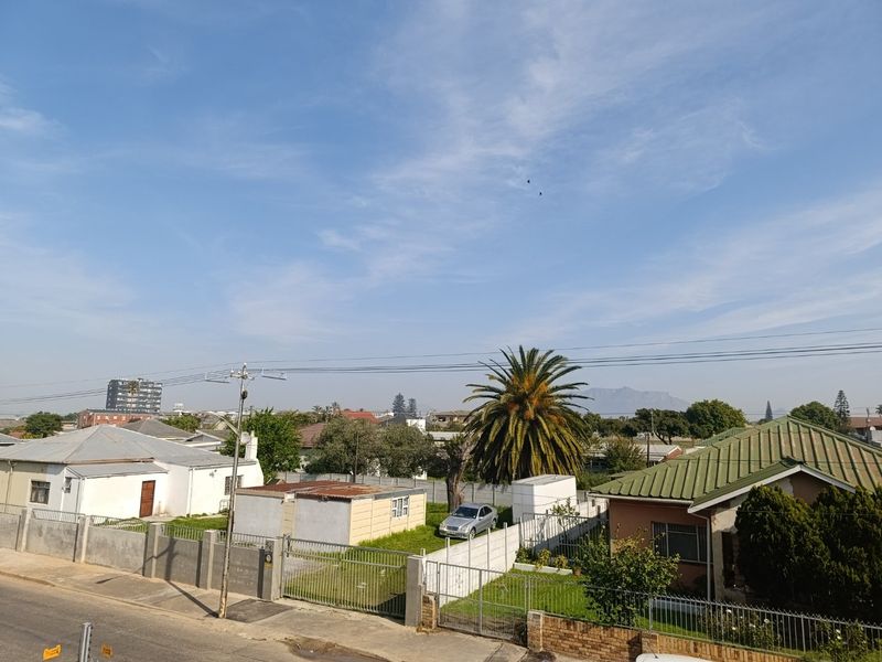 An elevated view overlooking a suburban residential neighborhood with surrounding houses, perimeter fencing, and distant mountain scenery under a clear blue sky.