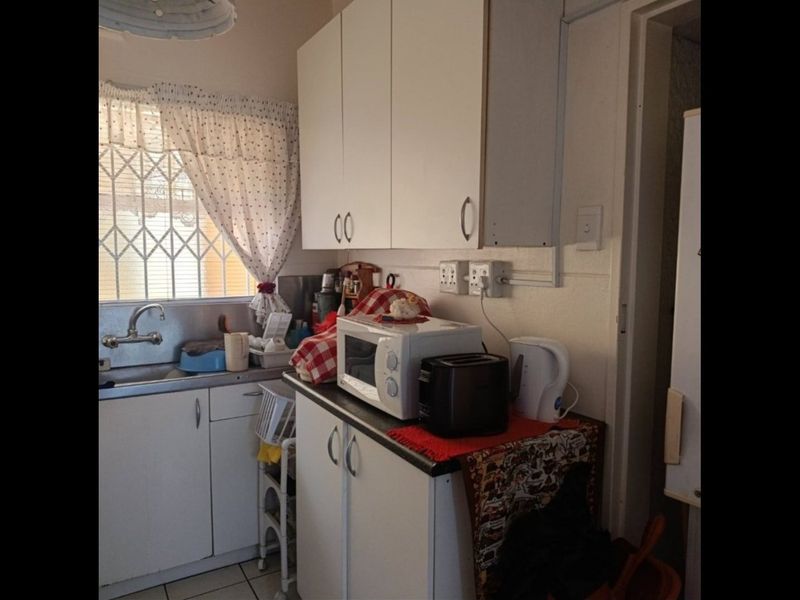 Compact kitchen featuring white cabinetry, laminate countertops, and a stainless steel sink, with a security gate over the window.