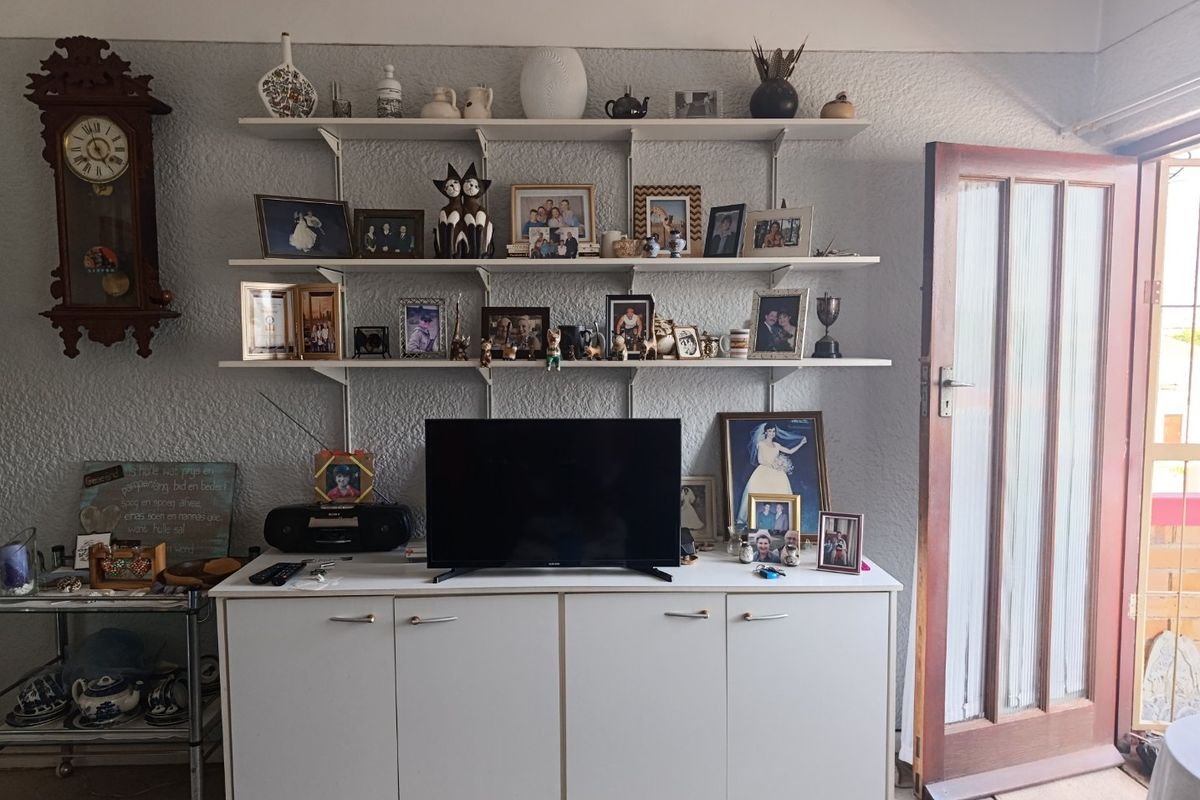 A living room area featuring built-in wall shelving and a white storage cabinet, with a timber-framed glass door leading to an outdoor space.