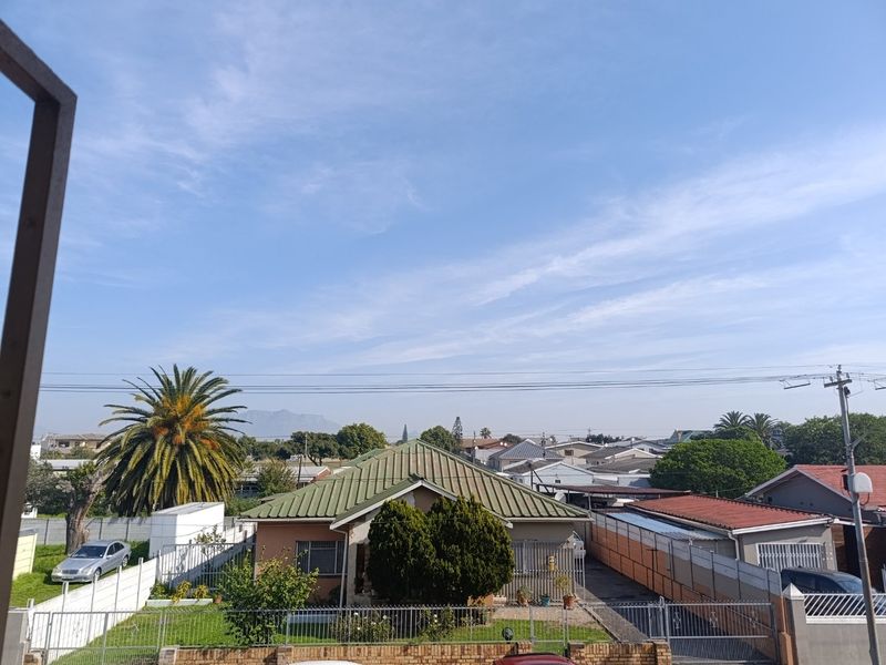 Elevated view overlooking a residential neighborhood with surrounding houses, mature trees, and distant mountain scenery.