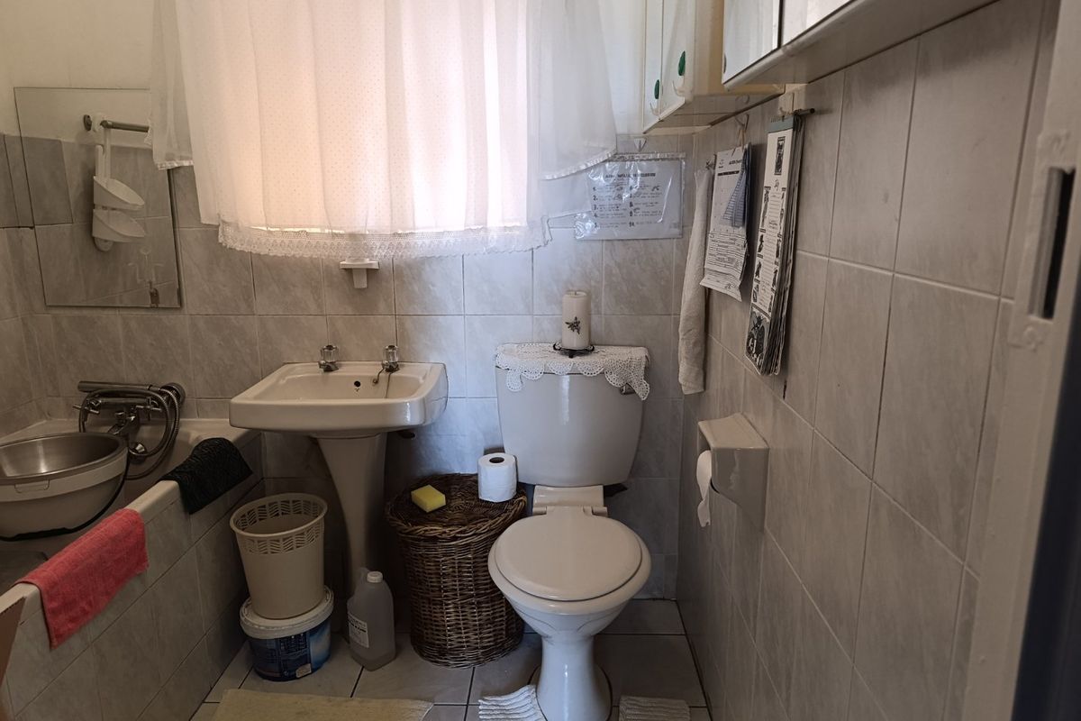 A compact bathroom featuring a pedestal basin, toilet, and bathtub with full-height wall tiling and a wall-mounted medicine cabinet.