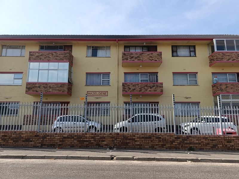 Front elevation of Hazeldene apartment complex featuring a brick and painted facade with enclosed balconies and secure perimeter fencing.
