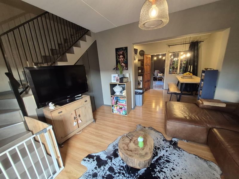 Open plan living and dining area featuring laminate flooring, a staircase with metal balustrade, and direct access to an adjacent room.