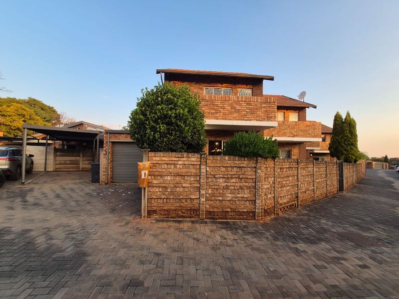 Front exterior view of a face brick townhouse featuring a paved driveway, covered carport, garage, and an upper-level balcony.