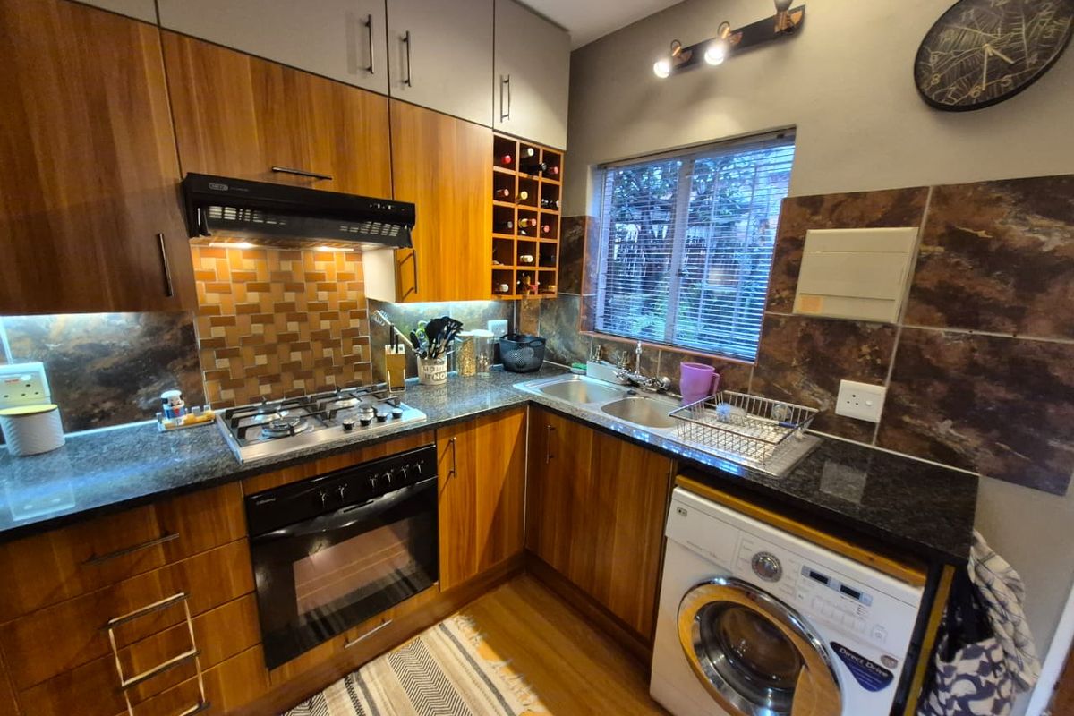 A well-appointed kitchen featuring wood-finish cabinetry, granite countertops, a gas hob with extractor, and integrated space for a washing machine.