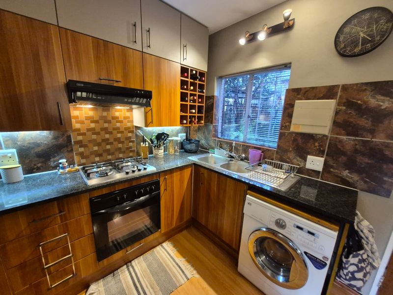 A well-appointed kitchen featuring wood-finish cabinetry, granite countertops, a gas hob with extractor, and integrated space for a washing machine.