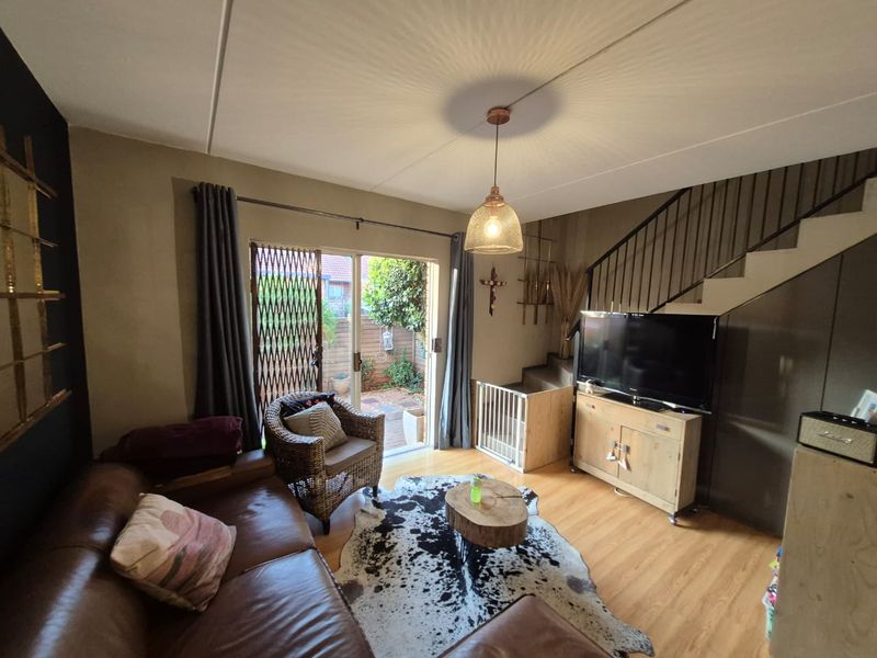 A cozy living room featuring laminate flooring, a staircase with metal railings, and a sliding glass door providing access to the rear patio area.