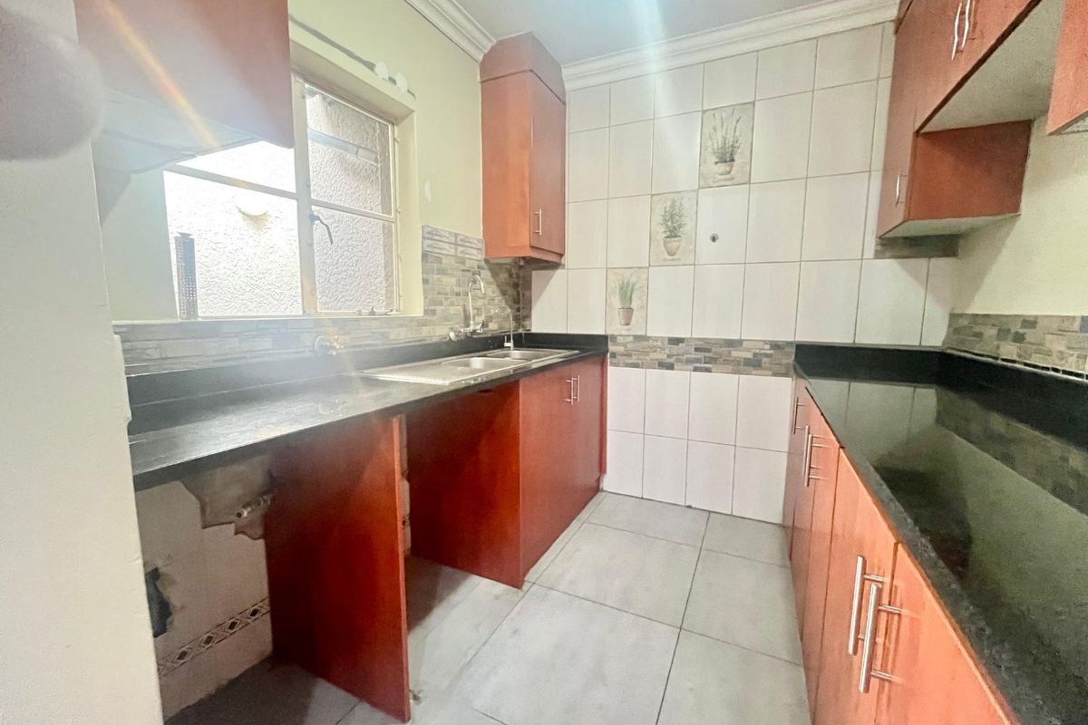 A compact kitchen featuring dark granite countertops, wooden cabinetry, and tiled finishes, currently requiring minor repairs and updates to the cabinetry and wall surfaces.