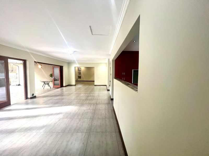 Spacious open-plan living area featuring neutral tiled flooring, recessed lighting, and a convenient pass-through window connecting to the kitchen area.