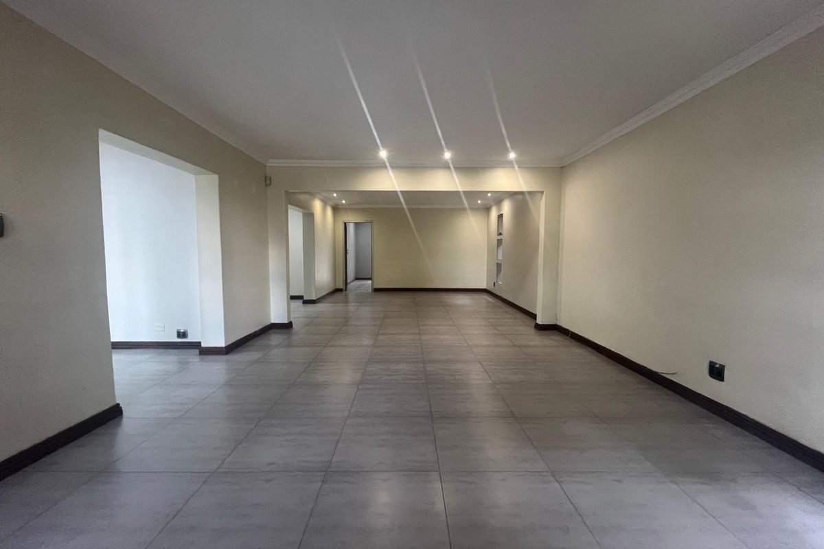 A spacious, empty living area featuring neutral walls, large format floor tiles, and recessed ceiling lighting, offering a versatile open-plan layout.